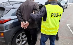 Policjant prowadzi zatrzymanego mężczyznę.