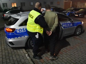 Policjant prowadzi zatrzymanego mężczyznę.