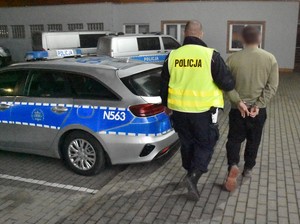 Policjant prowadzi zatrzymanego mężczyznę.