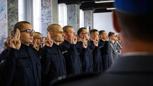 Nowi policjanci podczas ślubowania stoją z uniesioną prawą dłonią i wyprostowanymi palcami.