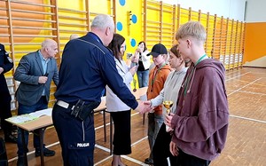 Szkolna sala gimnastyczna. Oficjalne zakończenie turnieju BRD. Policjant wręcza medal zwycięzcom turnieju.