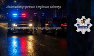 Policjanci stoją przy radiowozie z włączonymi światłami błyskowymi. Obok, po prawej stronie stoi zaparkowane audi. W tle widać mroczny obraz ulicy. Biały napis: Zlekceważył prawo i sądowe zakazy! Swoją bezmyślnością zagrażał innym.