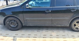 Czarny samochód osobowy. Przednie koło wymienione na zapasowe o stalowej feldze, tylne opona założona na feldze aluminiowej.