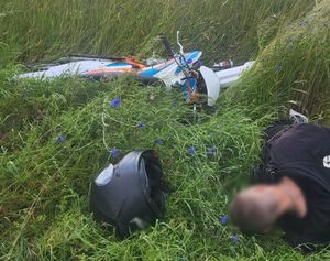 Motocyklista leżący na trawie po wywrotce. W pobliżu przewrócony motocykl i kask.