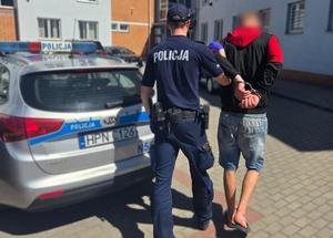 Policjant prowadzi zatrzymanego mężczyznę.