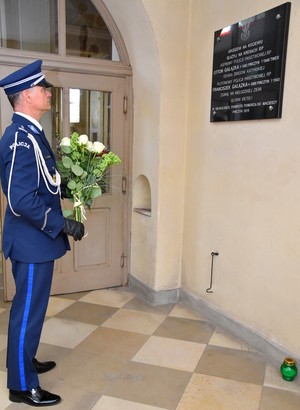 Komendant składa kwiaty przy tablicy upamiętniającej pomordowanych policjantów.