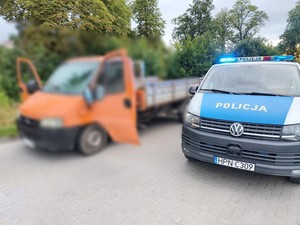 Radiowóz policyjny przy kontrolowanym aucie. Policyjne auto ma włączone światła błyskowe.