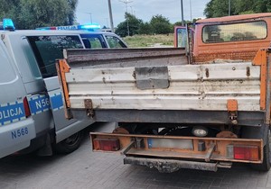 Radiowóz policyjny przy kontrolowanym aucie. Policyjne auto ma włączone światła błyskowe.