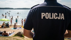 Policjant przygląda się osobom wypoczywającym nad jeziorem.