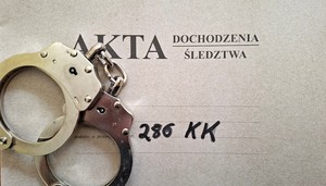 szara kartka z napisem akta sprawy art.286KK i na niej srebrne kajdanki