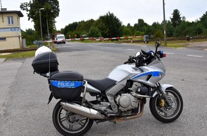 Na pierwszym planie policyjny motocykl, a w tle szlaban kolejowy.