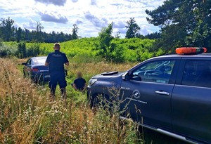 Policjant pilnuje zatrzymanego mężczyzny. Po prawej stronie pojazd służbowy nadleśnictwa.