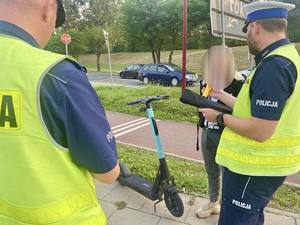 Policjanci pracują na miejscu zdarzenia z udziałem osoby kierującej hulajnogą lub wykonują czynności w ramach nadzoru nad ruchem.