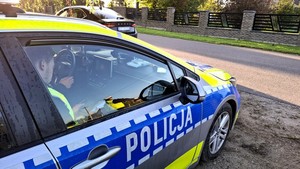 Na pierwszym planie bok radiowozu policyjnego, a za nim auto osobowe koloru ciemnego, które zostało zatrzymane do kontroli drogowej.