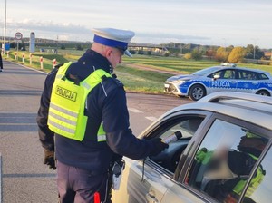Policjant kontroluje alkomatem trzeźwość kierowcy siedzącego w aucie.