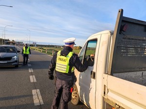 Policjant kontroluje alkomatem trzeźwość kierowcy siedzącego w aucie.