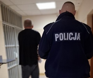 Policjant stoi z zatrzymanym przed drzwiami prowadzącymi do celi.