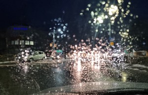 Widok drogi w nocy przez mokrą szybę w czasie opadu deszczu. Po lewej stronie znajduje się budynek komendy z niebieskim napisem Policja.