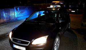 Zatrzymany przez policjantów ford w świetle niebieskich świateł błyskowych radiowozu.
