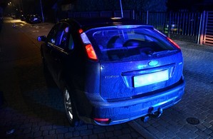 Zatrzymany przez policjantów ford w świetle niebieskich świateł błyskowych radiowozu.
