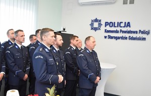 Na pierwszym planie policjanci w mundurach galowych, a w tle niebieski napis Komenda Powiatowa Policji w Starogardzie Gdańskim.