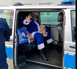 Niebieski Mikołaj siedzi w radiowozie, który ma otwarte drzwi.