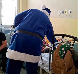 Mikołaj kładzie prezent na łóżko małego pacjenta.