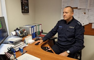 Policjant siedzi przy biurku, przed komputerem.