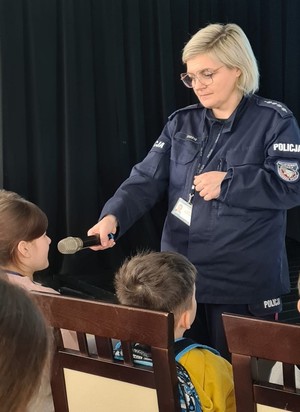 Policjantka prowadzi spotkanie z dziećmi w sali widowiskowej osiedlowego domu kultury.