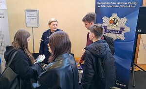 Policjantka rozmawia z młodzieżą w czasie Powiatowych Targów Edukacyjnych.