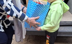 Kobieta przekazuje dziecku paczkę. Widoczne dłonie dorosłej osoby i dziecka przyjmującego słodycze.