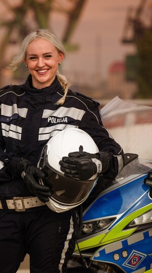 Policjantka z motocyklem. Kobieta trzyma przed sobą kask ochraniający głowę.
