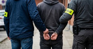 Kryminalni prowadzą zatrzymanego mężczyznę. Mężczyzna ma założone na rękach kajdanki. Zdjęcie obrazujące. wygenerowane przez AI.