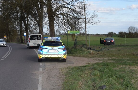 Droga. Na poboczu stoi radiowóz, a w oddali na polu stoi czarne Volvo.