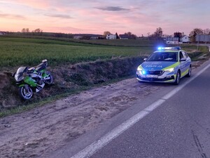 Zatrzymany do kontroli motocykl w rowie, a w tle radiowóz policyjny.