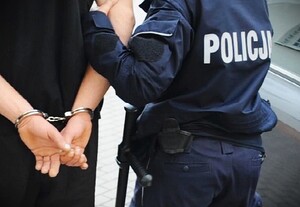 Policjant prowadzi zatrzymanego mężczyznę. Mężczyzna ma założone kajdanki. Zdjęcie ilustracyjne.