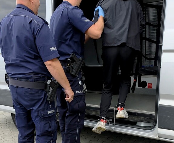 Policjanci wprowadzają zatrzymanego mężczyznę do radiowozu.