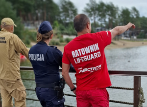 Policjant, strażak i ratownik stoją na pomoście przy kąpielisku.