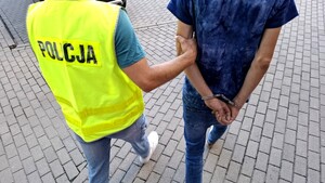 Policjant prowadzi zatrzymanego mężczyznę.