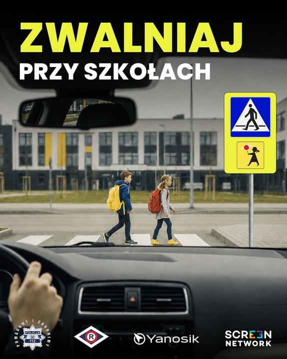 Dzieci z plecakami przechodzące przez przejście dla pieszych. W tle szkoła.
