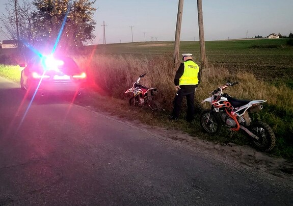 Nieoznakowany radiowóz z włączonymi światłami błyskowymi. Policjant stojący przy kontrolowanych motocyklach.